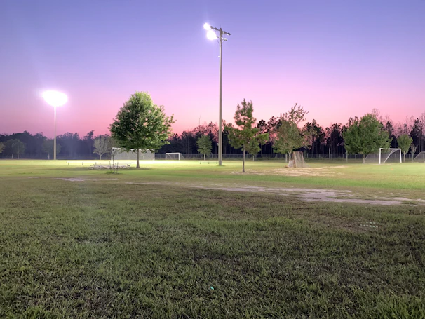 Wide shot of an open grassy field with people setting up for a soccer game at dawn