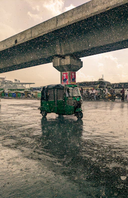 A mud-splashed rickshaw crossing a backwater bridge under a stormy Kerala sky.