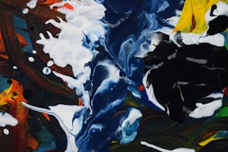 A vibrant abstract painting with swirling patterns dominated by deep blues, bright whites, and blacks, interspersed with hints of yellow and red. The paint appears to be poured and mixed, creating a fluid and dynamic composition.