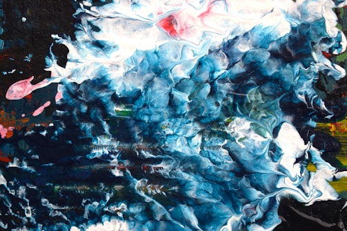A dynamic abstract painting featuring swirling and chaotic patterns in a predominantly blue color palette with splashes of white, black, and hints of red. The composition is fluid and appears to convey movement.