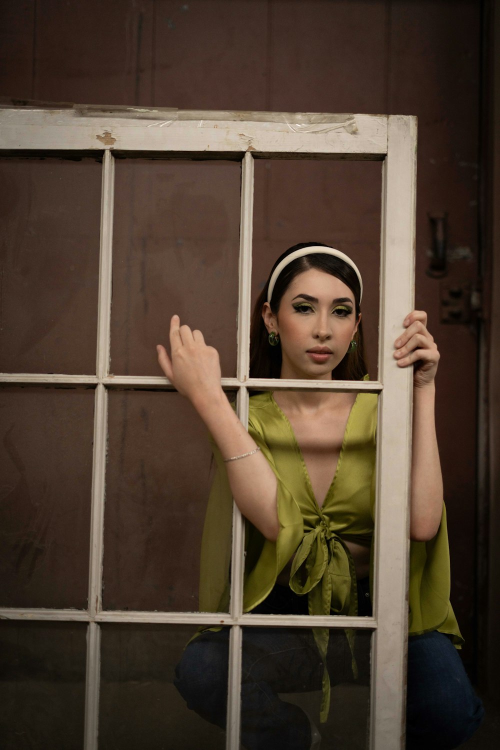 a woman is posing behind a window in a green top