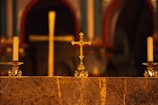 A warm-lit altar adorned with Syriac crosses and deep red cloths during a solemn service.