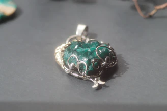 Artisan carefully setting a natural gemstone into a silver pendant, surrounded by tools and raw stones.