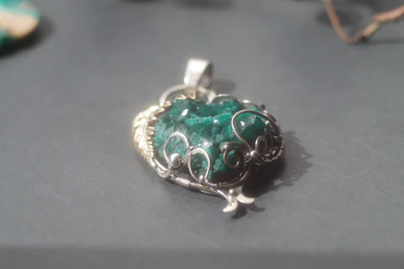 Artisan carefully setting a natural gemstone into a silver pendant, surrounded by tools and raw stones.