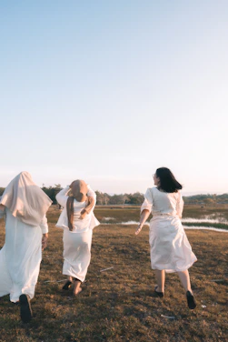 A serene scene of women in long flowing dresses and veils tending a cozy, sunlit garden, faces gently turned away.