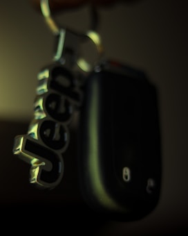 A close-up of a keychain with a metallic keyring attached to a black car key. The keychain features the word 'Jeep' in bold, metallic letters.