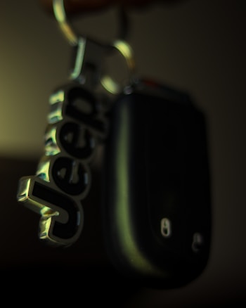 A close-up of a keychain with a metallic keyring attached to a black car key. The keychain features the word 'Jeep' in bold, metallic letters.