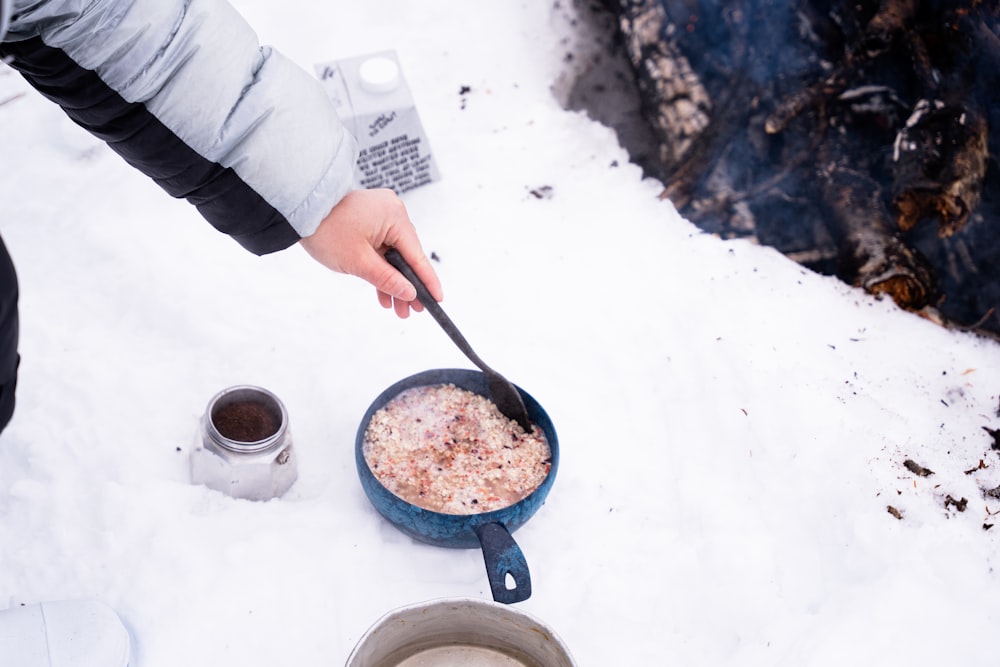 a person cooking food in a pan on a snowy surface