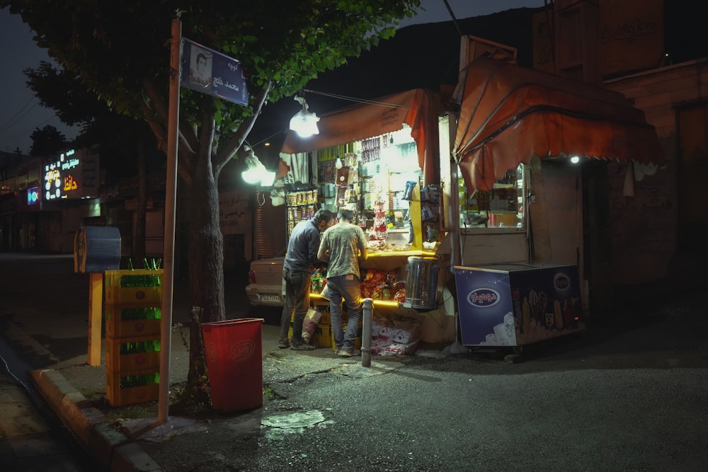 a couple of people standing outside of a food stand