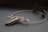 An elegant necklace with a unique design featuring a large, polished stone pendant. The stone is encased in intricate wirework that forms swirls and loops, giving it a sophisticated and artistic appearance. The necklace is displayed on a dark surface, and there are blurred floral elements in the background.