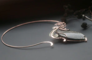 Elegant vintage necklace with pink gemstones displayed on a sage green velvet cushion.