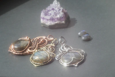 A set of rose gold pendants displayed on a wooden tray with natural lighting highlighting their shine