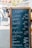A blackboard menu with wooden frame displays a list of food items and their prices in German at an outdoor market. In the background, people are walking past various market stalls and food trucks under a sunny sky.
