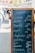 A blackboard menu with wooden frame displays a list of food items and their prices in German at an outdoor market. In the background, people are walking past various market stalls and food trucks under a sunny sky.