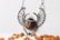 An intricate silver pendant shaped like a scarab beetle with wings, featuring a polished amber stone in the center. Small amber stones are scattered around on a white surface.