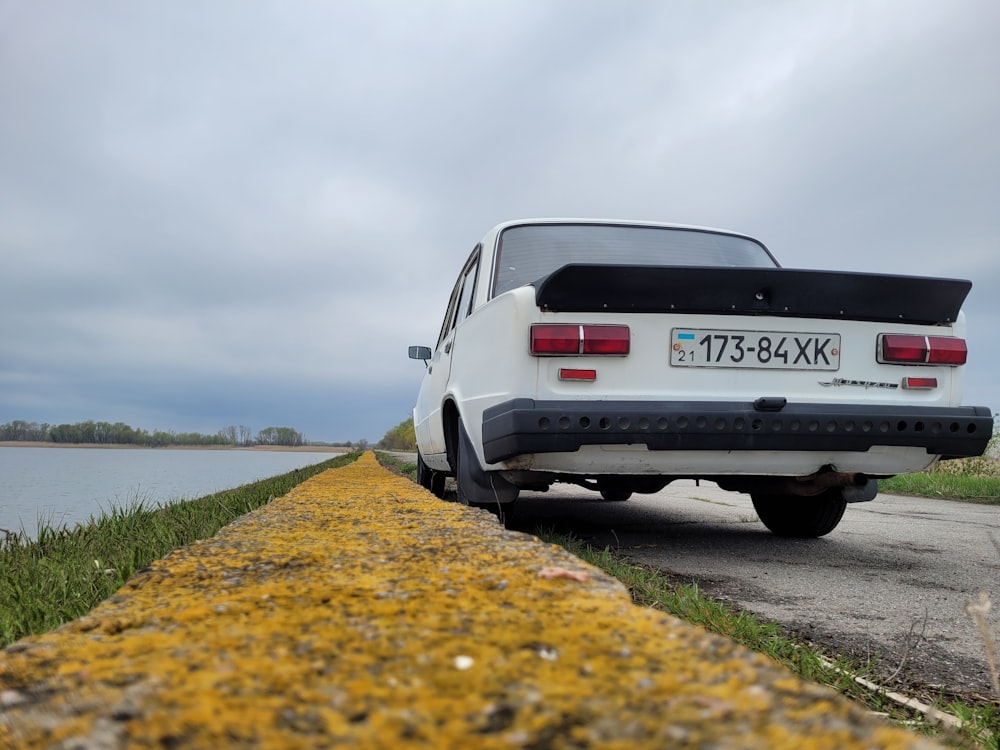 a white car parked on the side of a road next to a body of water