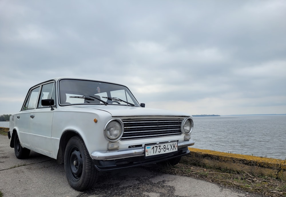 a white car parked on the side of a road next to a body of water