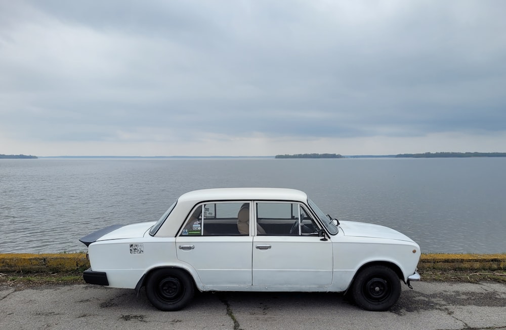 a white car parked on the side of a road next to a body of water