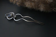A delicate gold hairpin with intricate detailing resting on a soft white background.