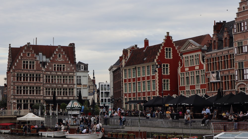 a group of people walking along a river next to tall buildings