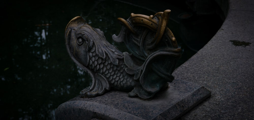 a statue of a fish on a ledge next to a body of water