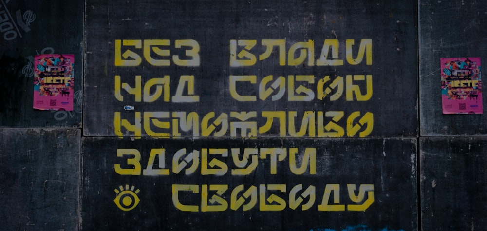 a black wall with yellow and pink graffiti on it