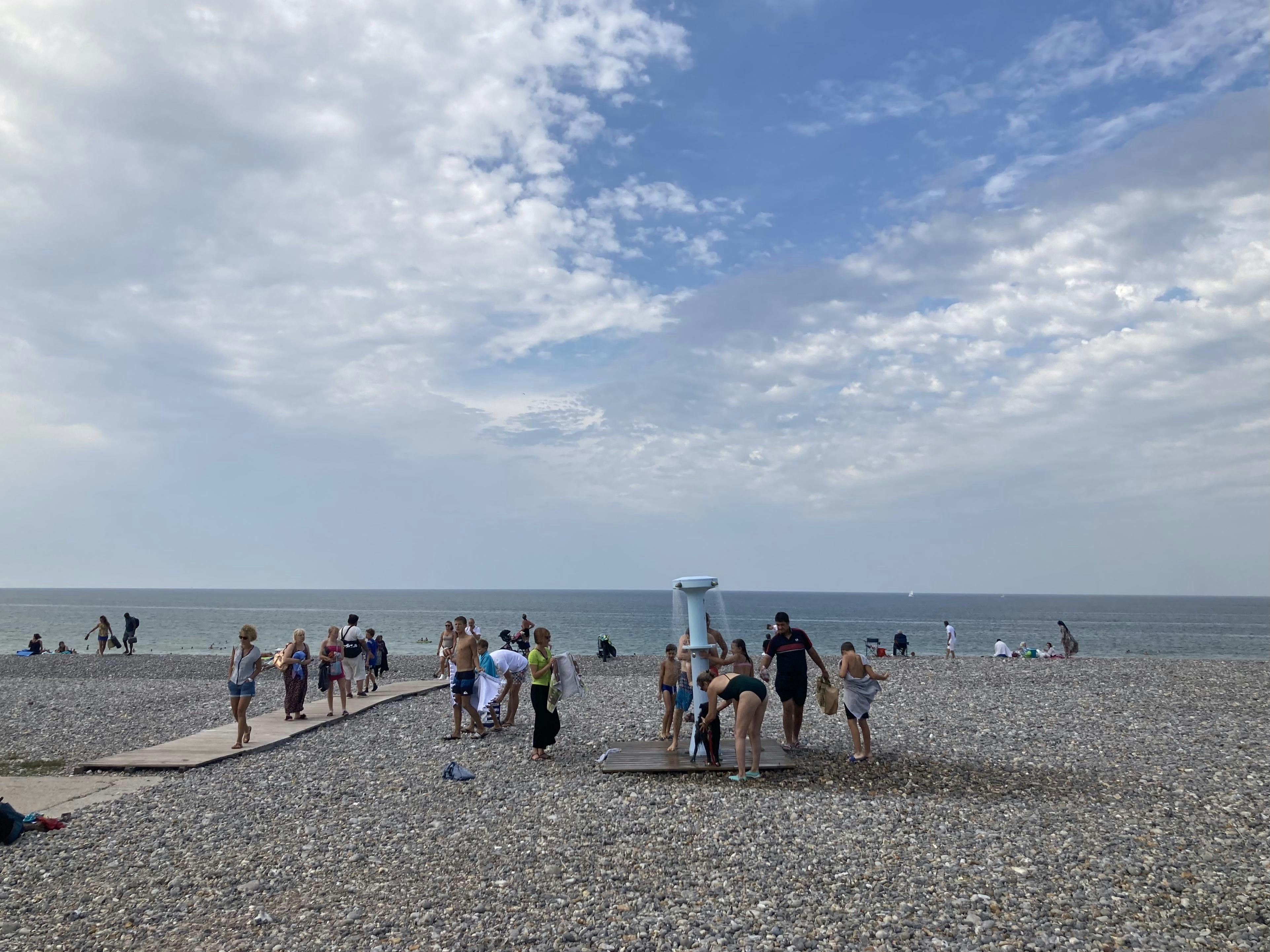 People showering and walking on a pebble beach by the sea.