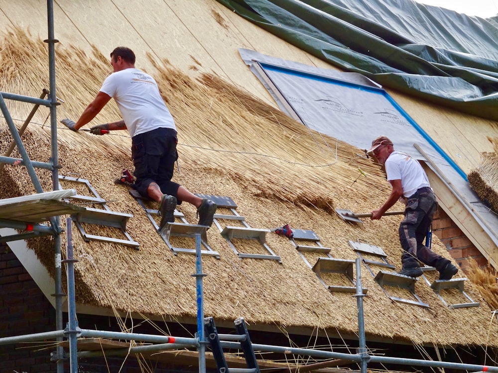 a couple of men working on a straw roof