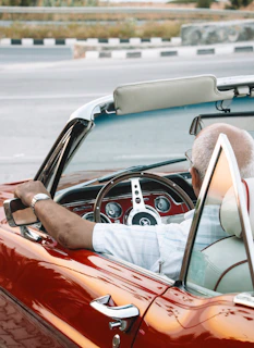 a man driving a red convertible car down a street
