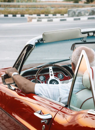 a man driving a red convertible car down a street