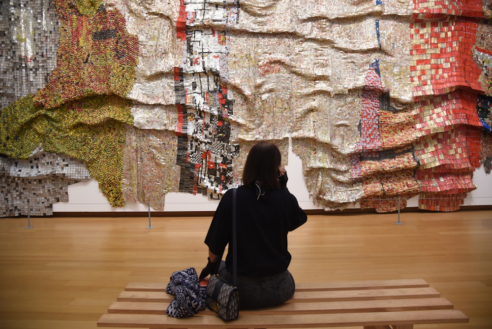 a woman sitting on a bench in front of a wall of fabric