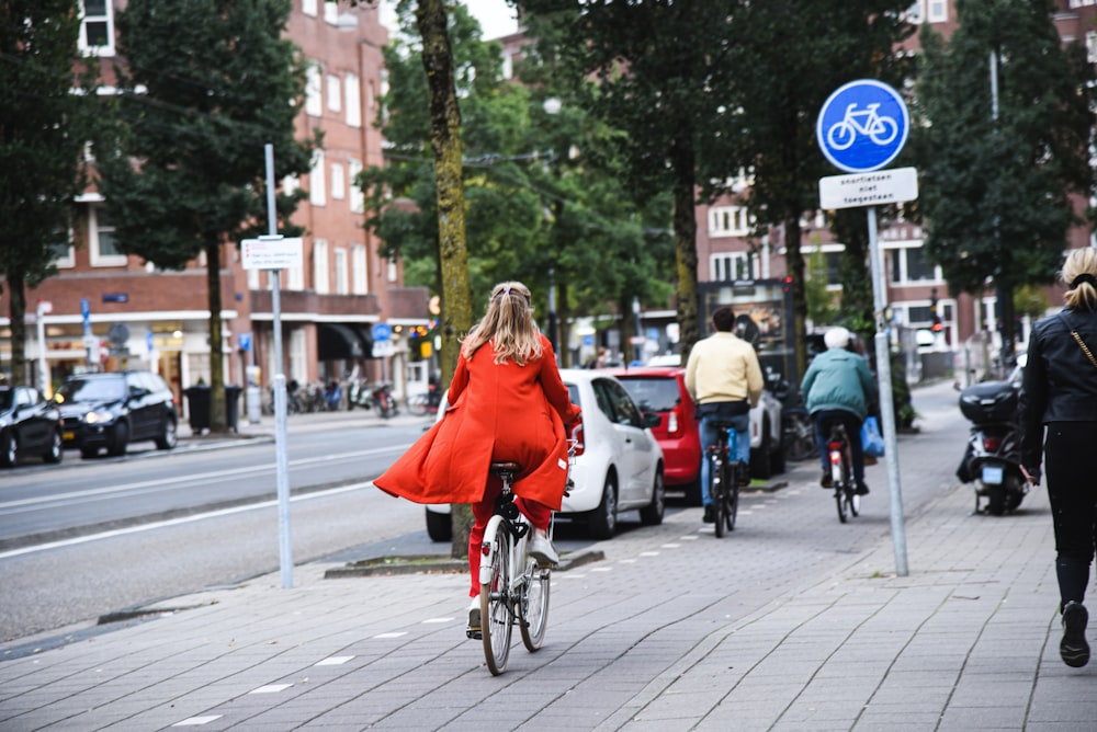 a woman in a red dress riding a bike down a street