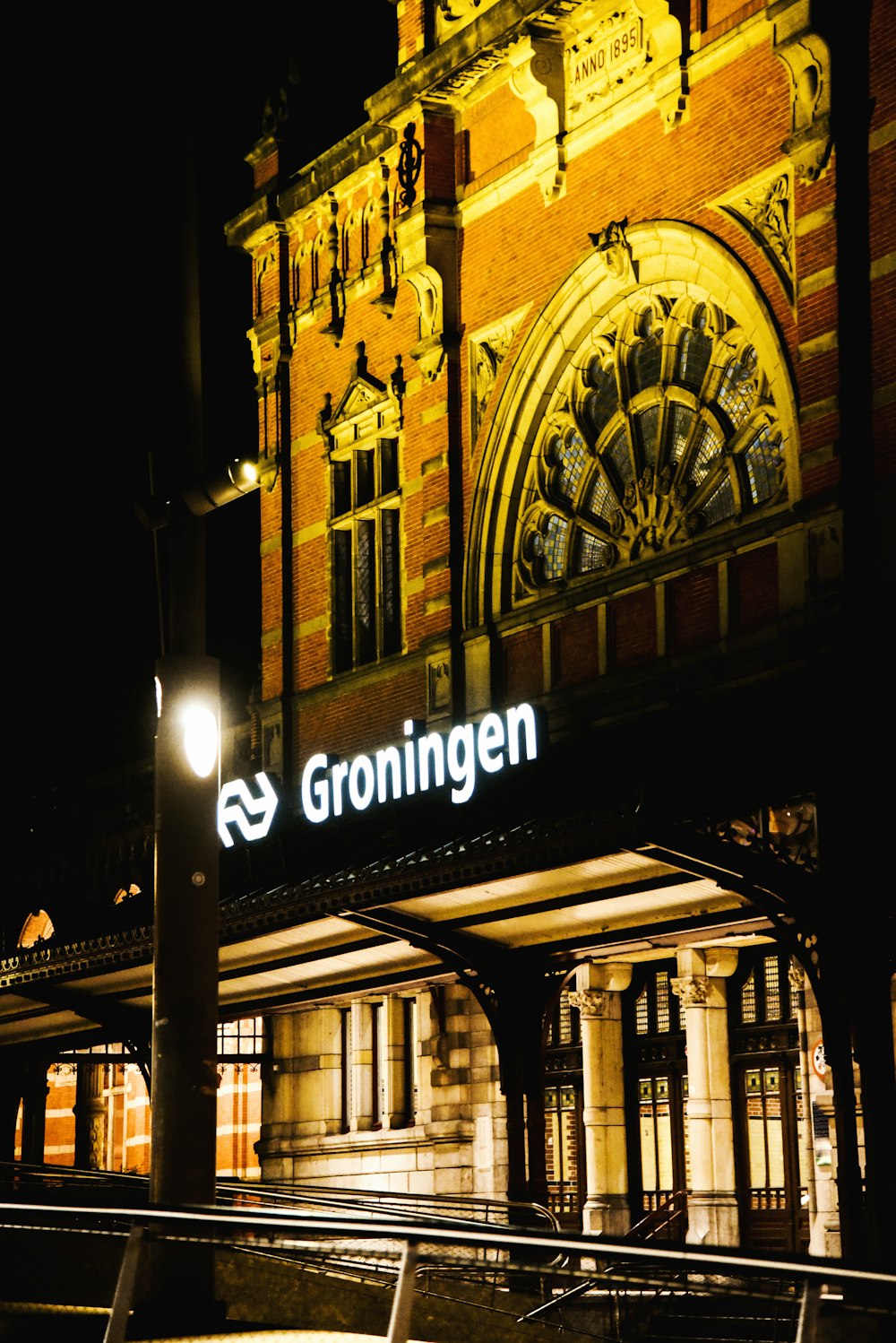 Una estación de tren por la noche con un gran edificio al fondo