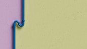 A blue pipe with an artistic bend is mounted on a two-tone wall. The wall features a lavender color on the left side and a light green color on the right. The pipe is secured with brackets and stands out against the muted background.