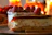 Close-up of a perfectly plated slice of rich cheesecake with golden crust and raspberry drizzle.
