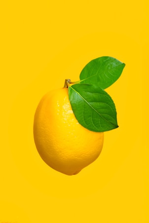 A vibrant yellow lemon with two green leaves attached, set against a solid yellow background, creating a bright and fresh visual contrast.