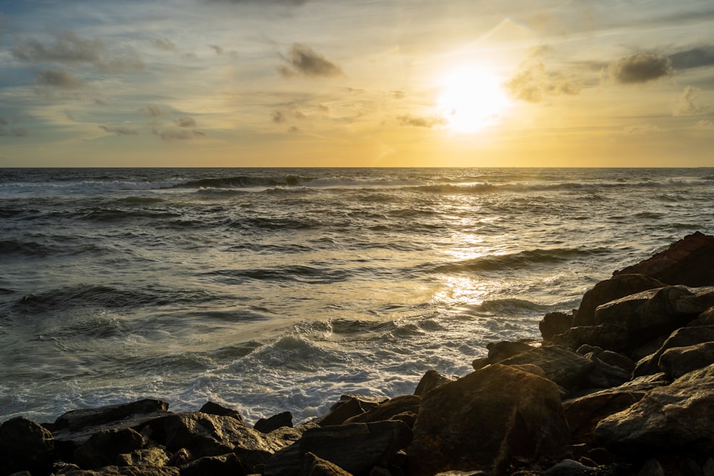 the sun is setting over the ocean on a rocky shore