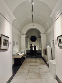 Visitors gently exploring an exhibit corridor with blue and white mosaic floors and framed artworks.
