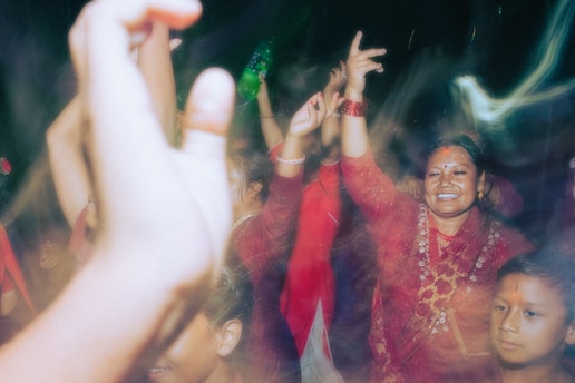 A group of people, mostly women, are dancing and celebrating. They are wearing traditional clothing and have joyful expressions on their faces. There are several raised hands and colorful outfits, indicating a lively and festive atmosphere.