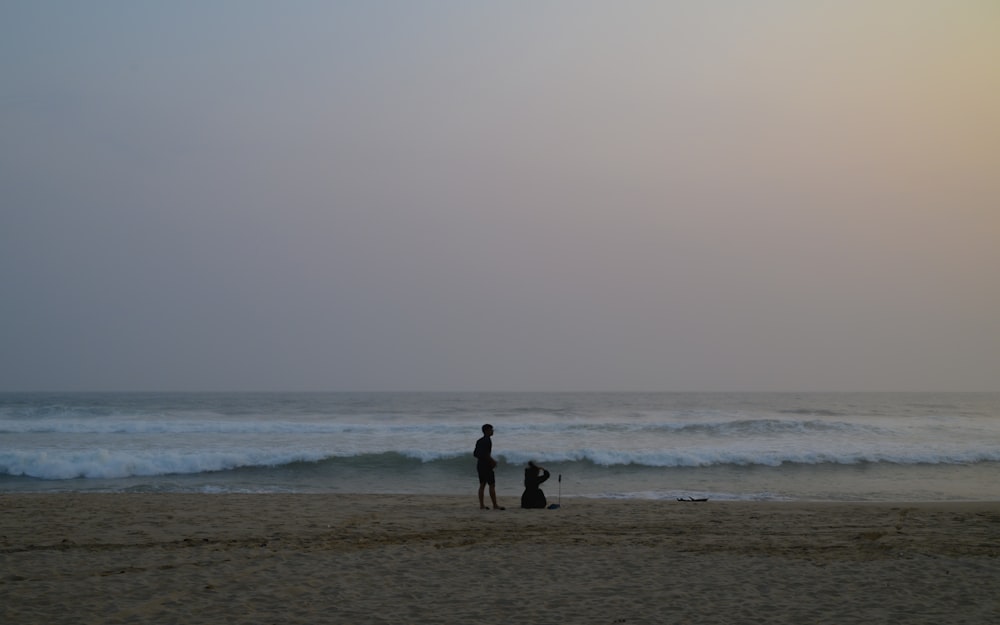 a couple of people standing on top of a sandy beach