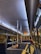 The interior of a dimly lit bus with several passengers seated. The lighting creates a warm and intimate ambiance, with reflections visible on the bus windows. There are metal poles for standing passengers and red cushioned seats arranged in rows.