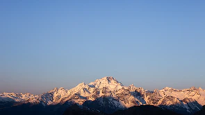 Majestic mountain peaks bathed in golden morning light with a clear blue sky.