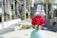A beautifully arranged outdoor seating area features elegant round tables with plush seating. In the foreground, a vase filled with vibrant red roses adds a burst of color against the neutral tones of the furniture. The backdrop consists of an ornate metal structure draped with black curtains and surrounded by greenery, creating a sophisticated and inviting ambiance.