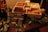 A wooden box contains separate compartments filled with marshmallows, graham crackers, chocolate, and a small can of fuel. Skewers are placed on top and a detailed guide for making s'mores is visible in front of the box. Green leaves are spread around the box for decoration.