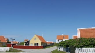 A cozy Bulgarian village street lined with traditional whitewashed houses and red-tiled roofs under a clear blue sky.
