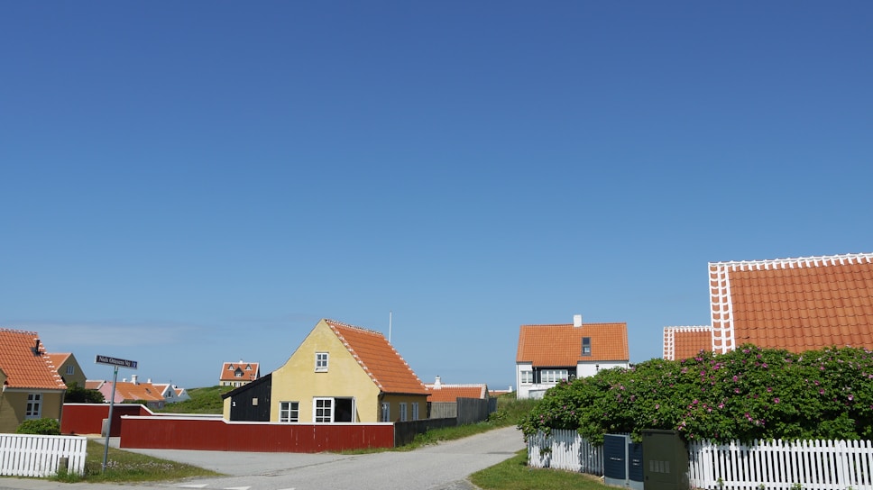 A cozy Bulgarian village street lined with traditional whitewashed houses and red-tiled roofs under a clear blue sky.