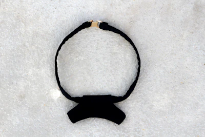A stylish black leather choker with subtle silver details on a white background.