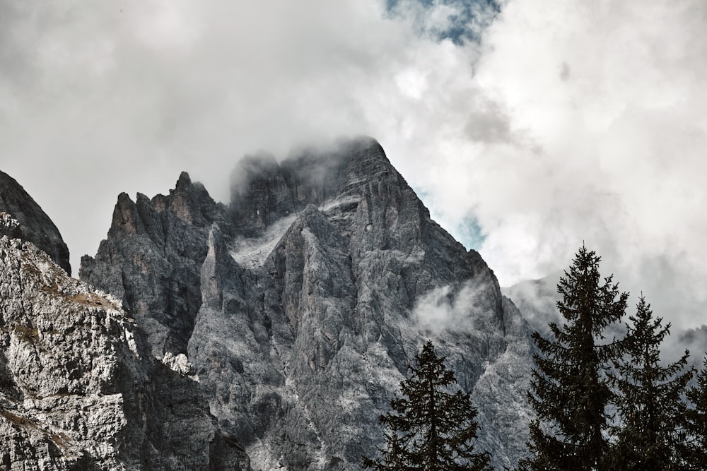 a mountain range with clouds and trees in the foreground