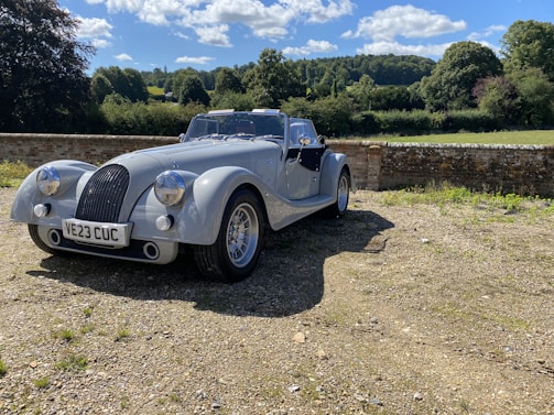 A vintage car parked by the villa’s ivy-covered stone wall under a clear blue sky.