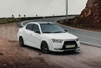 A sleek white sedan parked on a winding mountain road with lush greenery around.